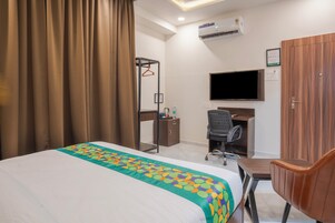 Habitación de hotel con cama, escritorio, silla, televisor y aire acondicionado.