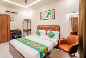 Habitación de hotel con una cama grande, cabecera de madera, un escritorio, una silla y un aire acondicionado instalado en la pared.
