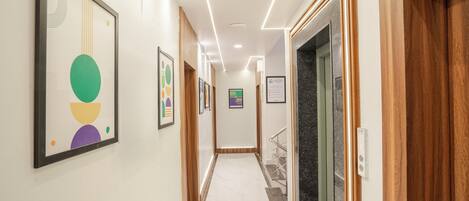 A hallway with framed artwork on the walls, a marble floor, and a staircase with a metal railing.