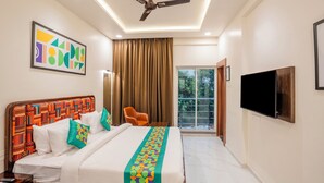 Quarto de hotel com uma cama, ventoinha no teto, televisão e janela com cortinas.