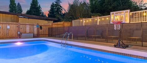 Une piscine dans le jardin, avec un panier de basketball et des chaises longues.