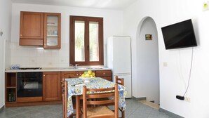Une cuisine avec des meubles en bois, un réfrigérateur blanc, une table à manger avec des chaises et un téléviseur fixé au mur.