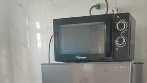 Ein Edelstahl-Kühlschrank mit integriertem Mikrowellenherd, platziert in einer Ecke mit gefliestem Boden.