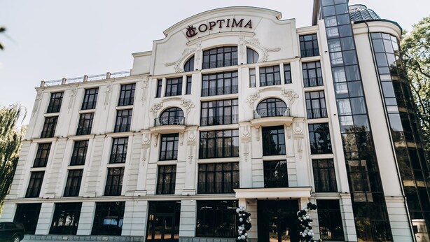 A large, white building with the name "OPTIMA" on the facade. It features multiple windows and balconies, with a curved corner section.