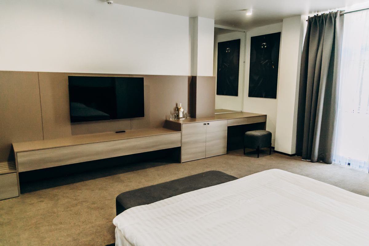 A modern hotel room with a large bed, a flat-screen TV, a desk, and a wardrobe.