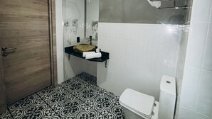 A bathroom with a wooden door, a sink with a towel holder, a toilet, and patterned floor tiles.