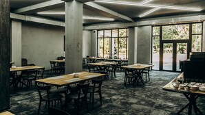 A spacious room with multiple tables and chairs, large windows, and a ceiling with linear lighting fixtures.