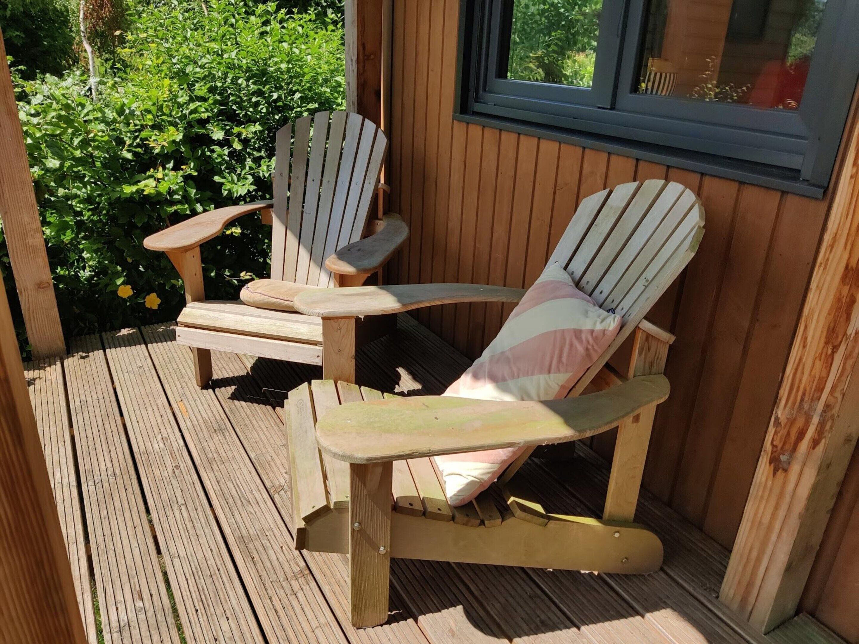 Dos sillas Adirondack en una terraza de madera con una ventana arriba.