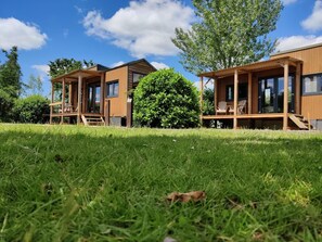 A modern wooden cabin with a deck and a large bush in the foreground. - Holiday Home in Netherlands for a Peaceful Retreat (Scherpenzeel)