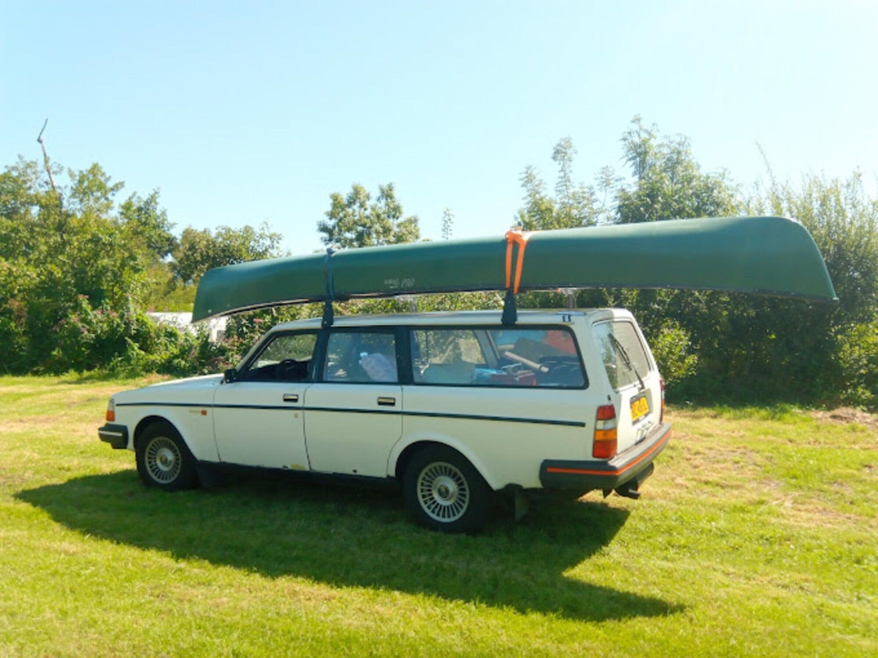 A white station wagon parked on grass with a green canoe on its roof.