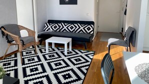A living room with a black and white patterned rug, a black sofa with patterned cushions, a white coffee table, and a wicker chair.