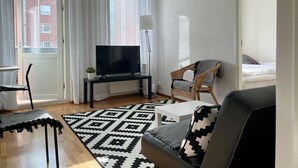 A modern living room with a flat-screen TV, a wicker chair, a sofa with a patterned throw, and a patterned rug.
