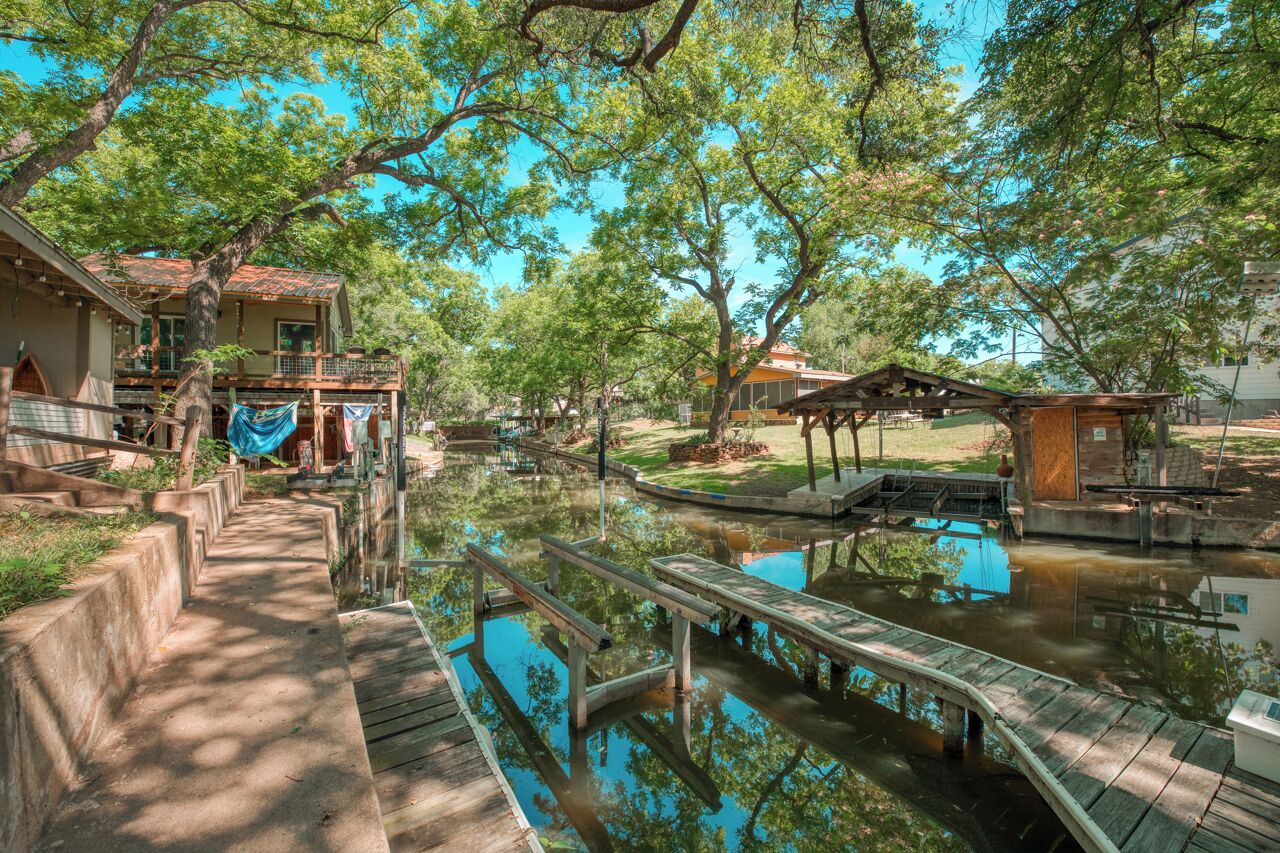 A riverside property with a wooden dock, a small bridge, and a house with a balcony overlooking the water.