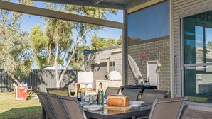 An outdoor patio with a table set for dining, surrounded by chairs, and a pizza oven in the background. - Break-A-Way COASTAL COMFORT IN LANCELIN (Lancelin)