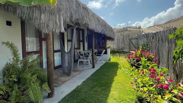 A thatched-roof house with a small porch, a lawn, and a wooden fence.