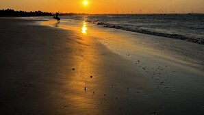 A beach at sunset with a person kiteboarding and wind turbines in the background.