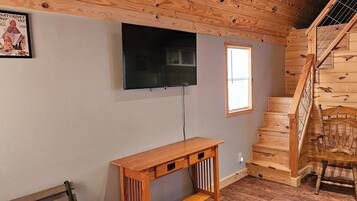 A room with a wooden staircase, a TV mounted on the wall, and a small wooden table.