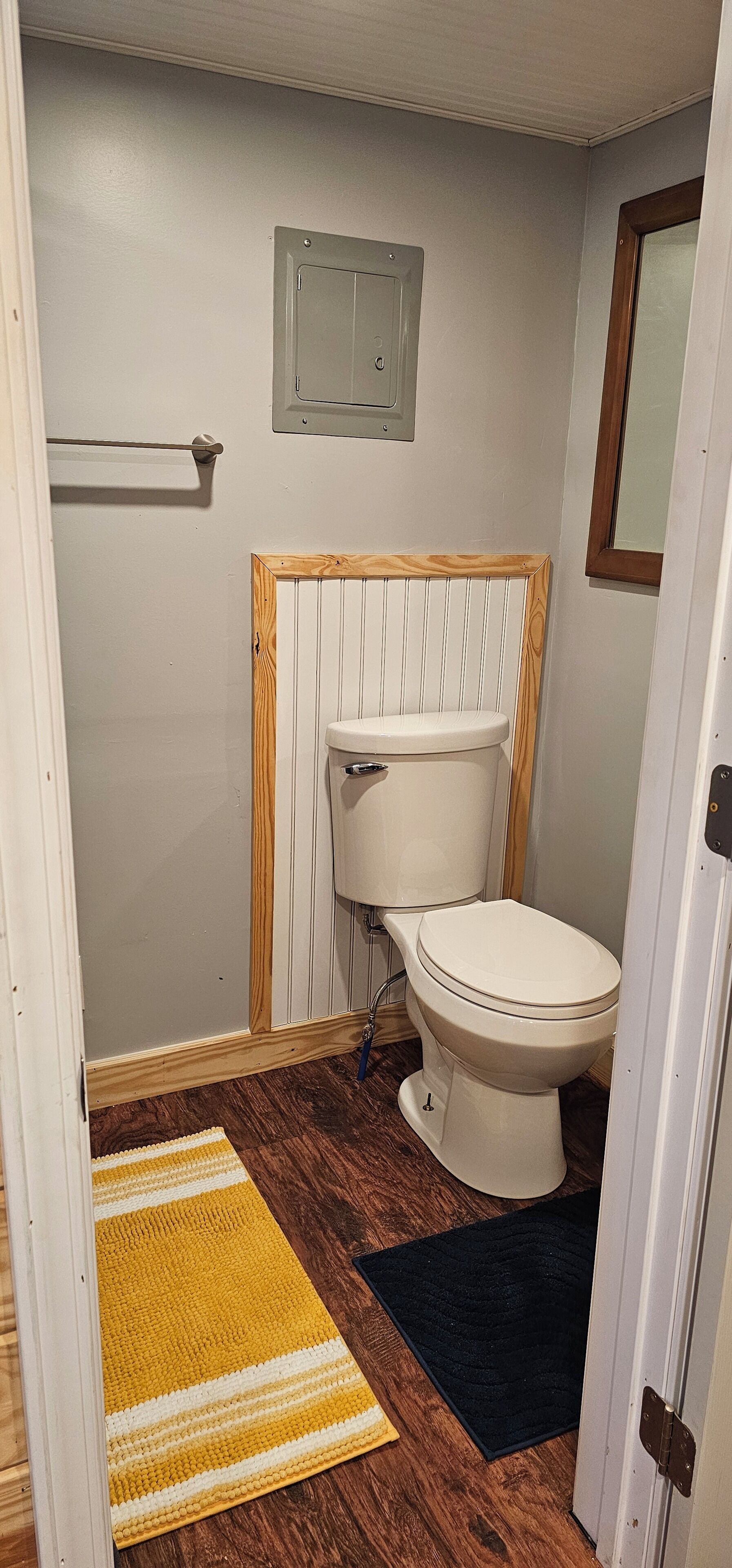 Une salle de bain avec des toilettes, un lambris en bois, un porte-serviettes et un tapis jaune et noir.