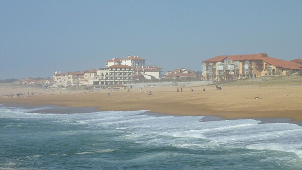 Un hotel frente a la playa con varias edificaciones, una playa de arena y el océano.