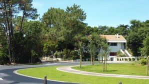 Un barrio residencial con una calle curva, un separador verde y una casa moderna con techo de tejas.