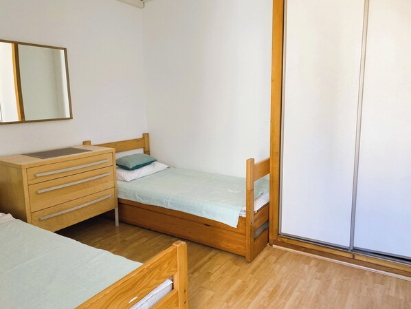 Una habitación pequeña con una cama individual, un tocador de madera, un espejo y una puerta corrediza.