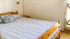 Un dormitorio con cama de madera, aire acondicionado blanco, un cuadro enmarco de una ola y una ventana con cortinas.