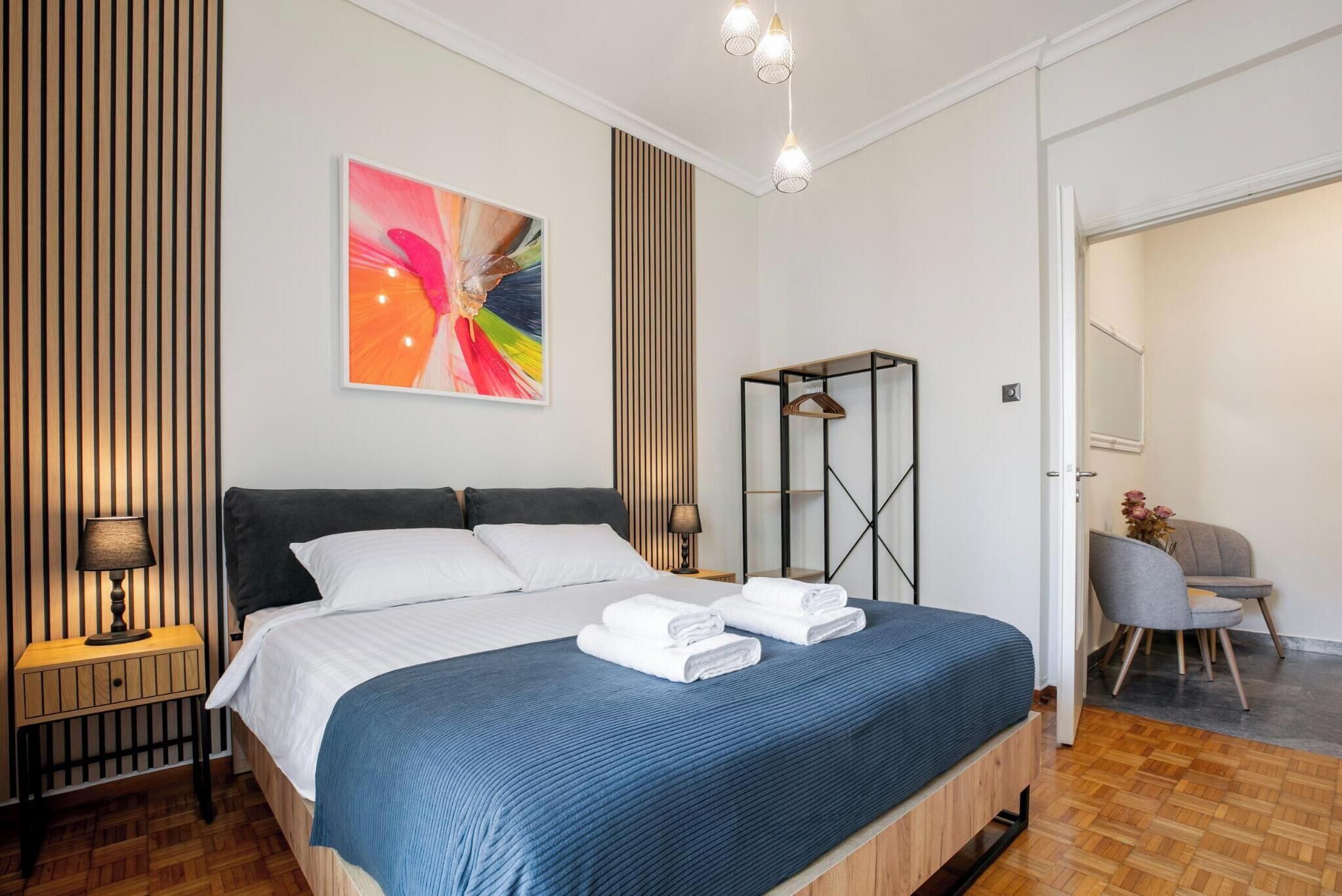 A modern hotel room with a large bed, a bedside table, a wall-mounted lamp, a mirror, and a chair.