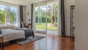 Une chambre dotée d’un grand lit, d’un bureau et offrant une vue sur un jardin grâce à une porte-fenêtre coulissante.