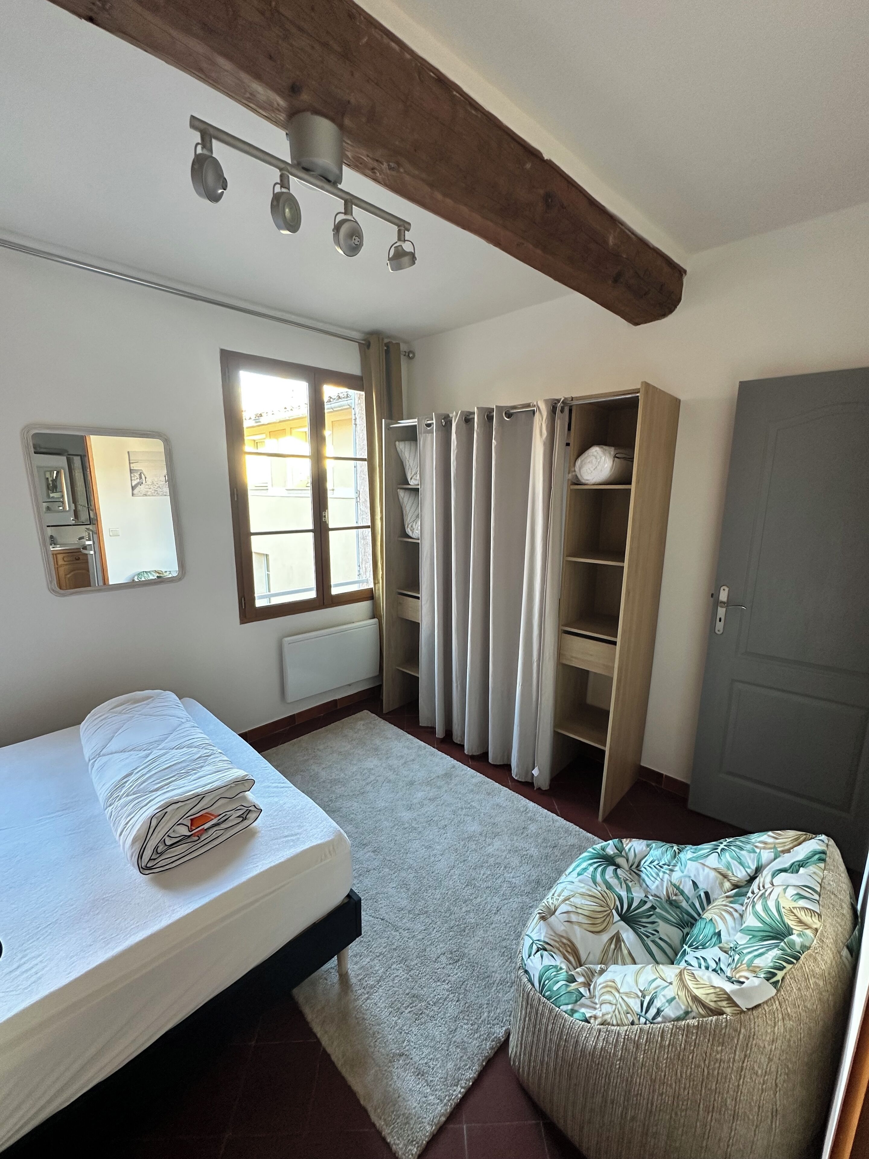 A bedroom with a bed, a small sofa, a wardrobe, and a window with curtains.