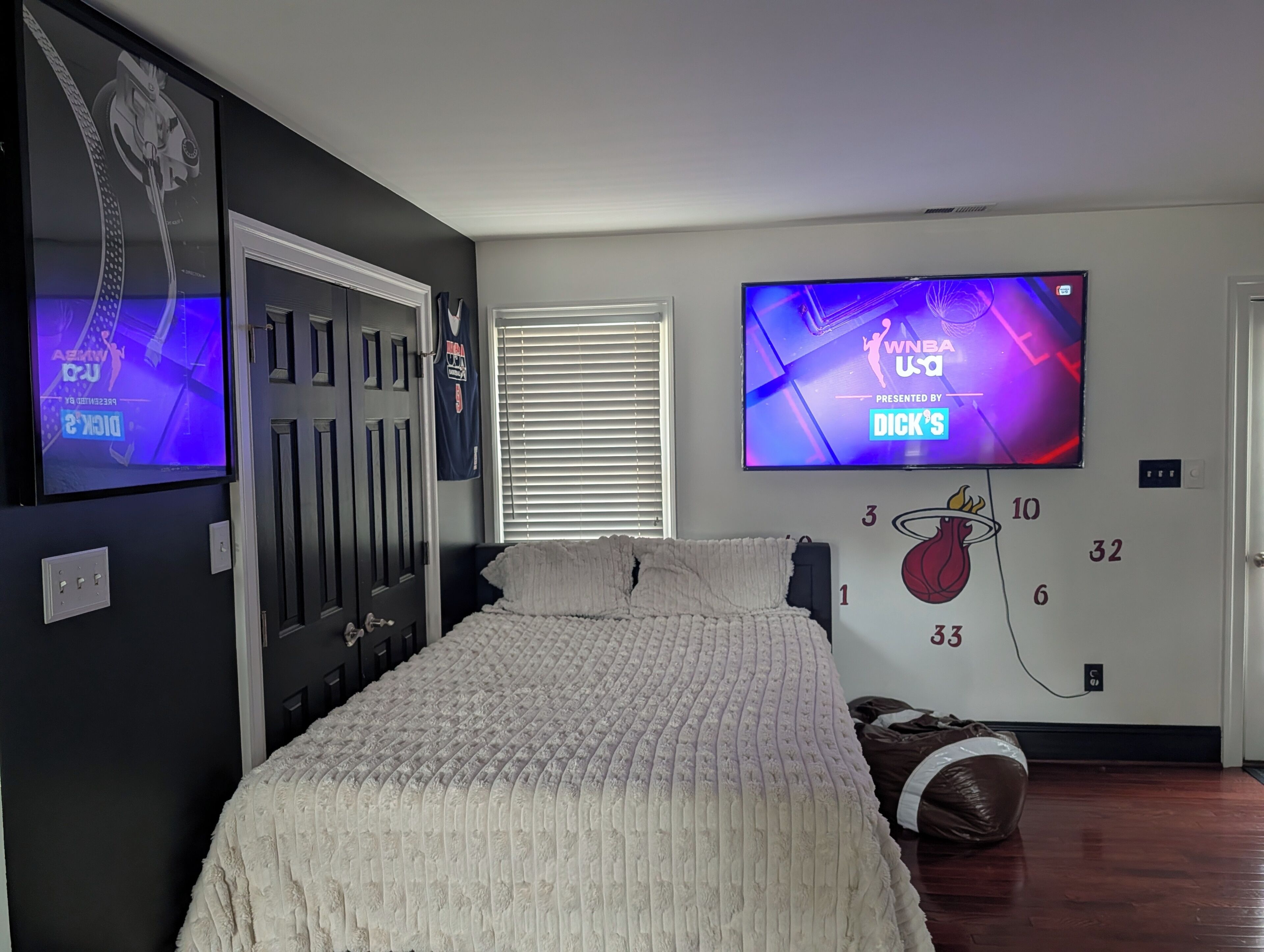 Camera da letto con un letto, una TV a parete, un adesivo a forma di canestro da basket e una porta con serratura.