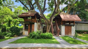 A rustic cabin with a wooden staircase connecting two levels, surrounded by lush greenery and a clear sky. - Seven 50s (Pai)