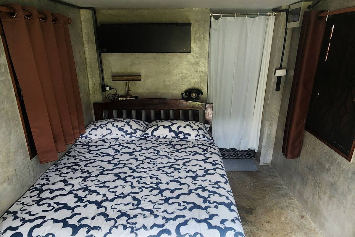A bedroom with a bed, curtains, a radiator, and a small table.
