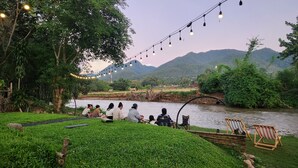 A riverside seating area with string lights, greenery, and a view of distant hills. - Seven 50s (Pai)