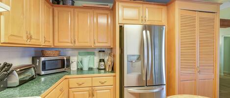A kitchen with wooden cabinets, a stainless steel refrigerator, a microwave, and a sink.
