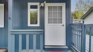 Una casa blu con porta e finestra bianca, un piccolo portico e una recinzione in legno.