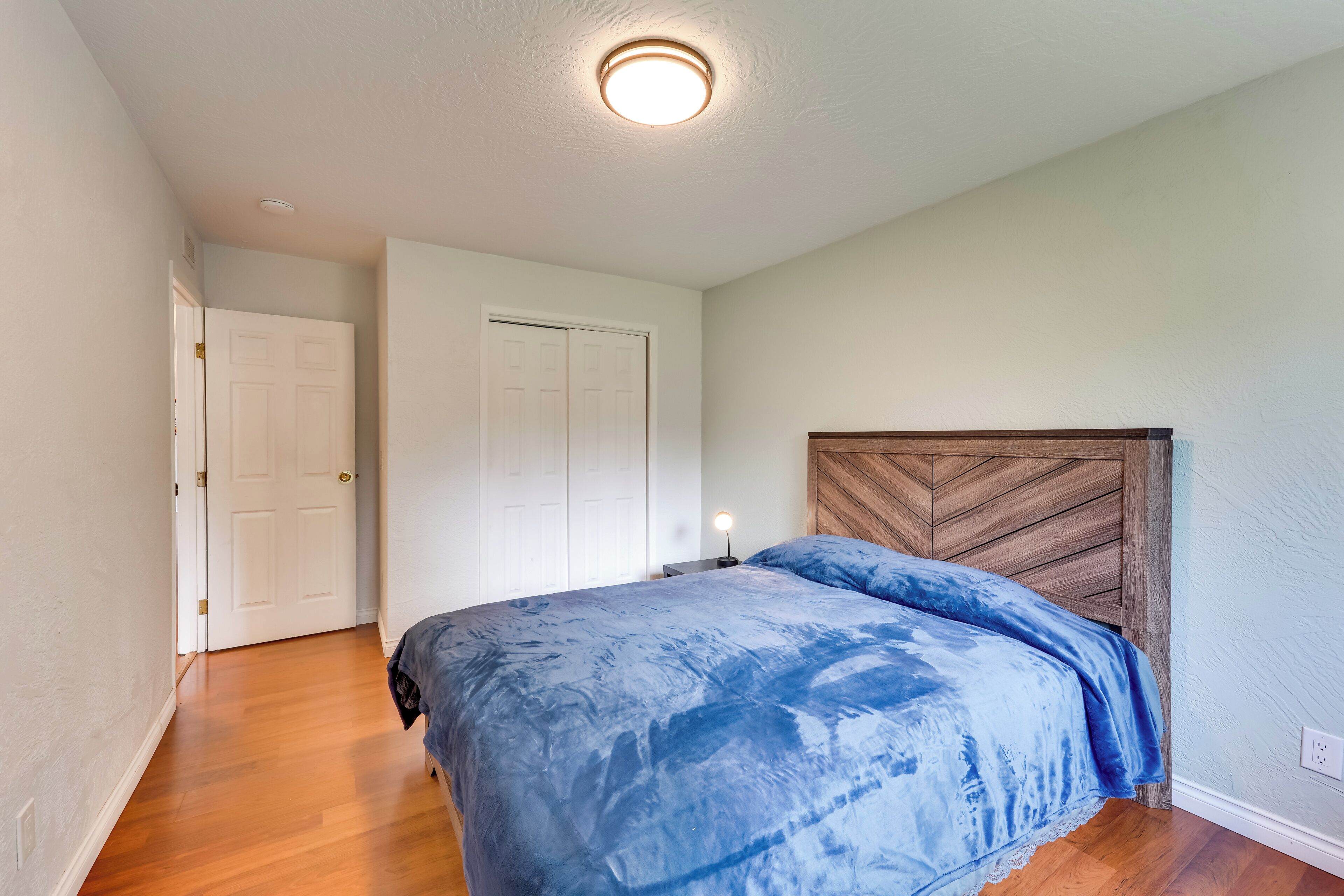 A bedroom with a bed, wooden headboard, white walls, and a door.
