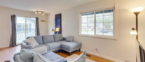 A modern living room with a sectional sofa, a flat-screen TV, and a large window providing natural light.