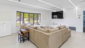 A modern living room with a beige sectional sofa, a small wooden table, and a TV mounted on the wall. - Home 6 Mi to Hollywood Beach: Grill, Swim, Relax (Hollywood)