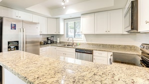 A modern kitchen with white cabinets, granite countertops, stainless steel appliances, and a window providing natural light. - Walk to Ocean & Golf: North Myrtle Beach Home! (North Myrtle Beach)