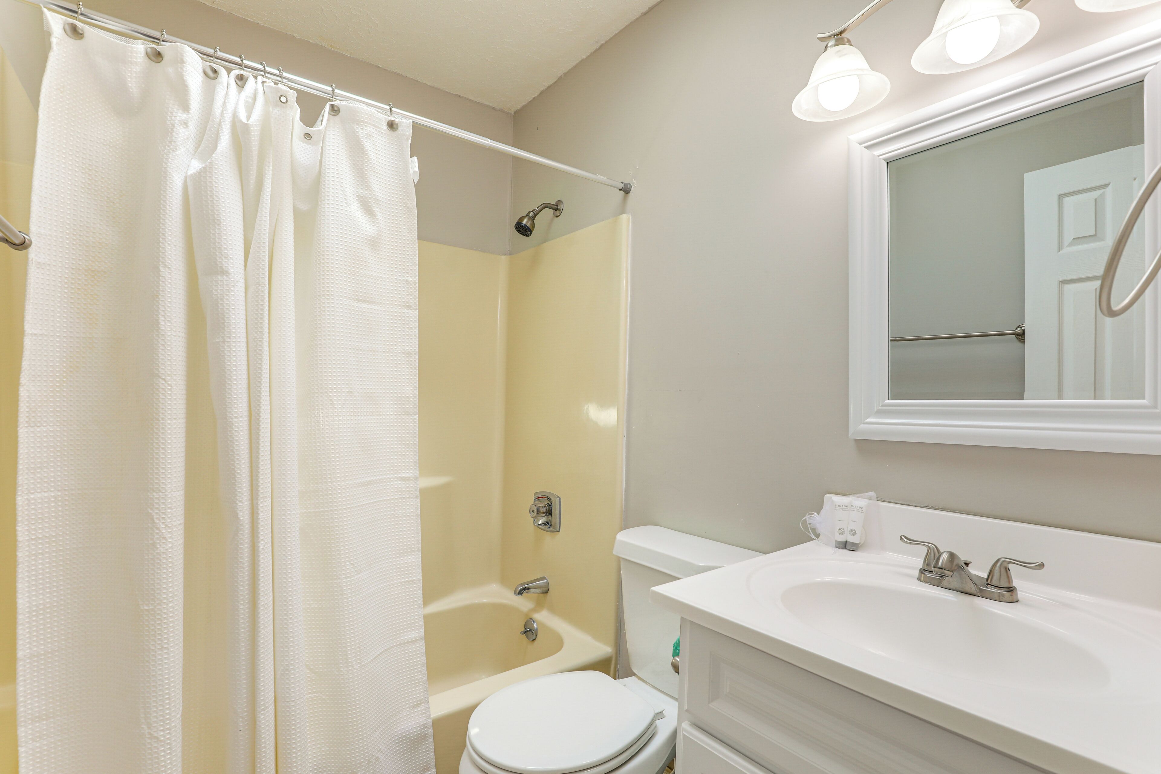 A bathroom with a shower, toilet, sink, and mirror.