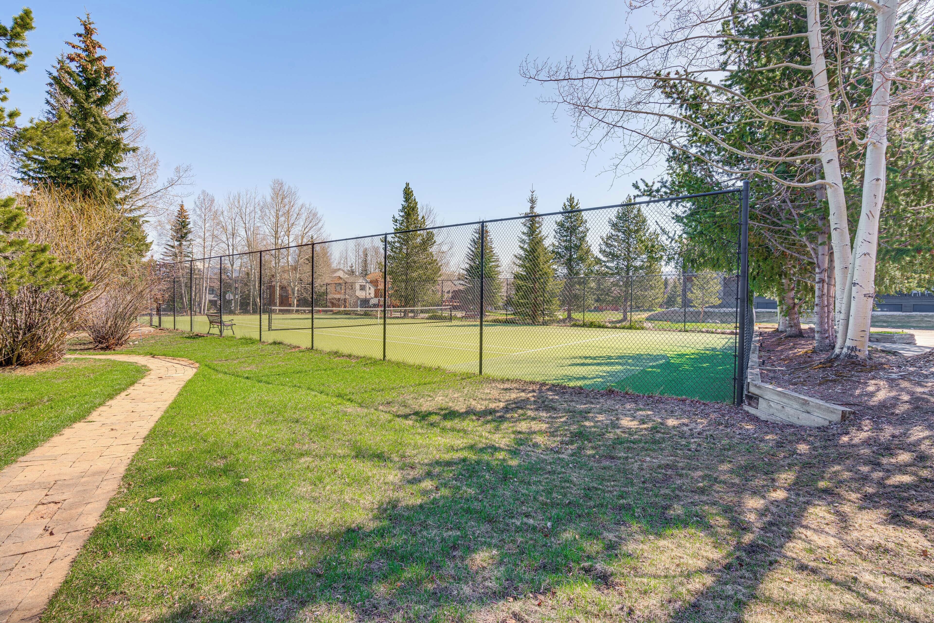Een omheind buitengebied met een geplaveid pad, omgeven door bomen en gras.
