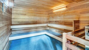 Een houten sauna met banken en een klein zwembadgedeelte.