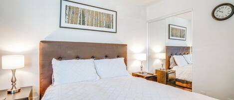 A hotel room with a large bed, two bedside tables with lamps, a wall clock, and a framed picture above the bed.