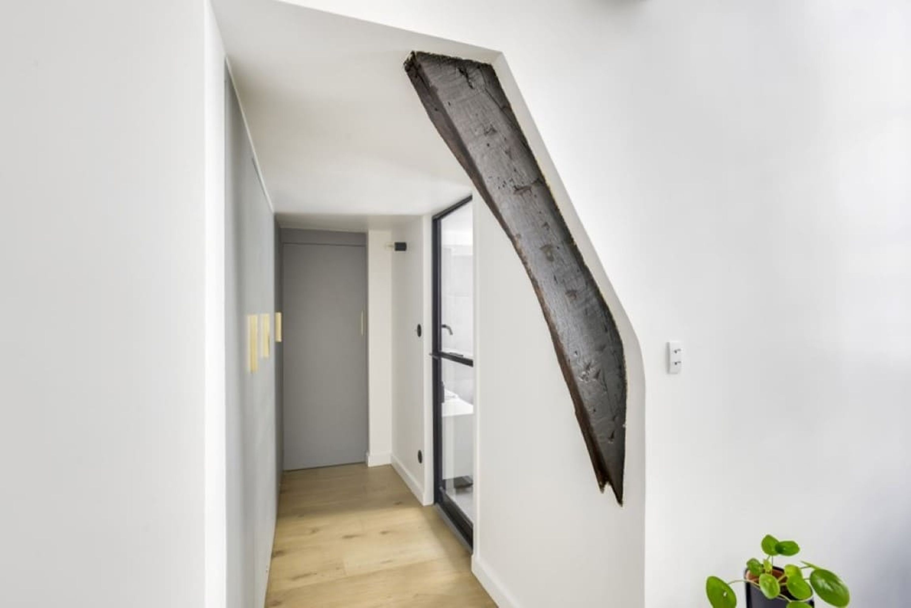 A hallway with a wooden floor, a white wall, and a large, dark, curved wooden beam.