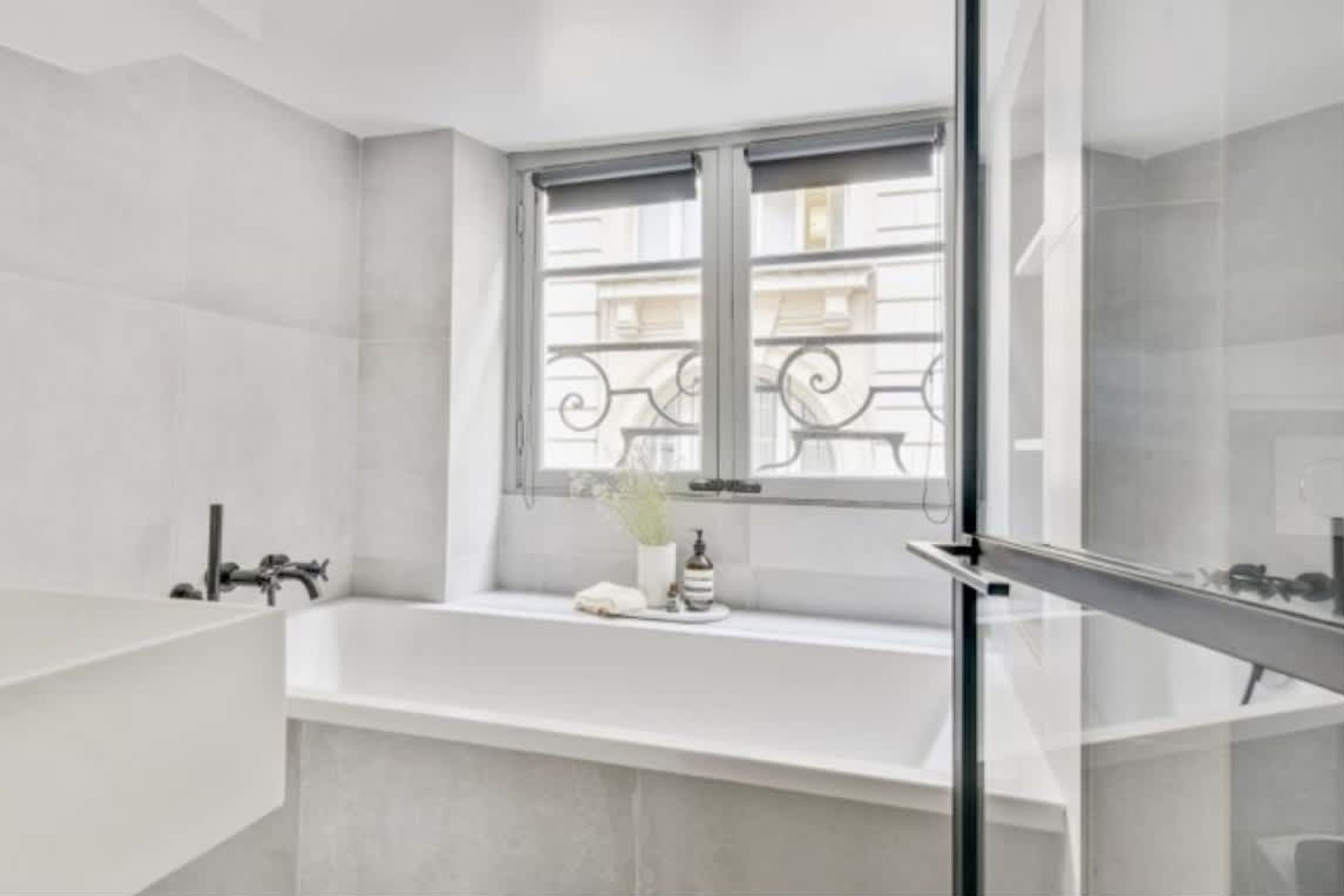 A modern bathroom with a freestanding bathtub, a window with decorative iron railings, and a glass shower enclosure.