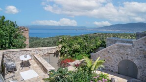 A stone terrace with outdoor furniture, a view of the sea, and surrounding greenery. - Niki s Tower - Majestic Seaview Stone Nest (Kalamata)