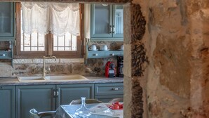A rustic kitchen with a stone archway, wooden cabinets, and a dining table with chairs. - Niki s Tower - Majestic Seaview Stone Nest (Kalamata)