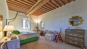 A bedroom with a bed, bedside table, lamp, chair, dresser, and a mirror on the wall. - New Historic Tuscany Country House Retreat in a Vineyard Near Siena Villa Chiantissimo (Castelnuovo Berardenga)