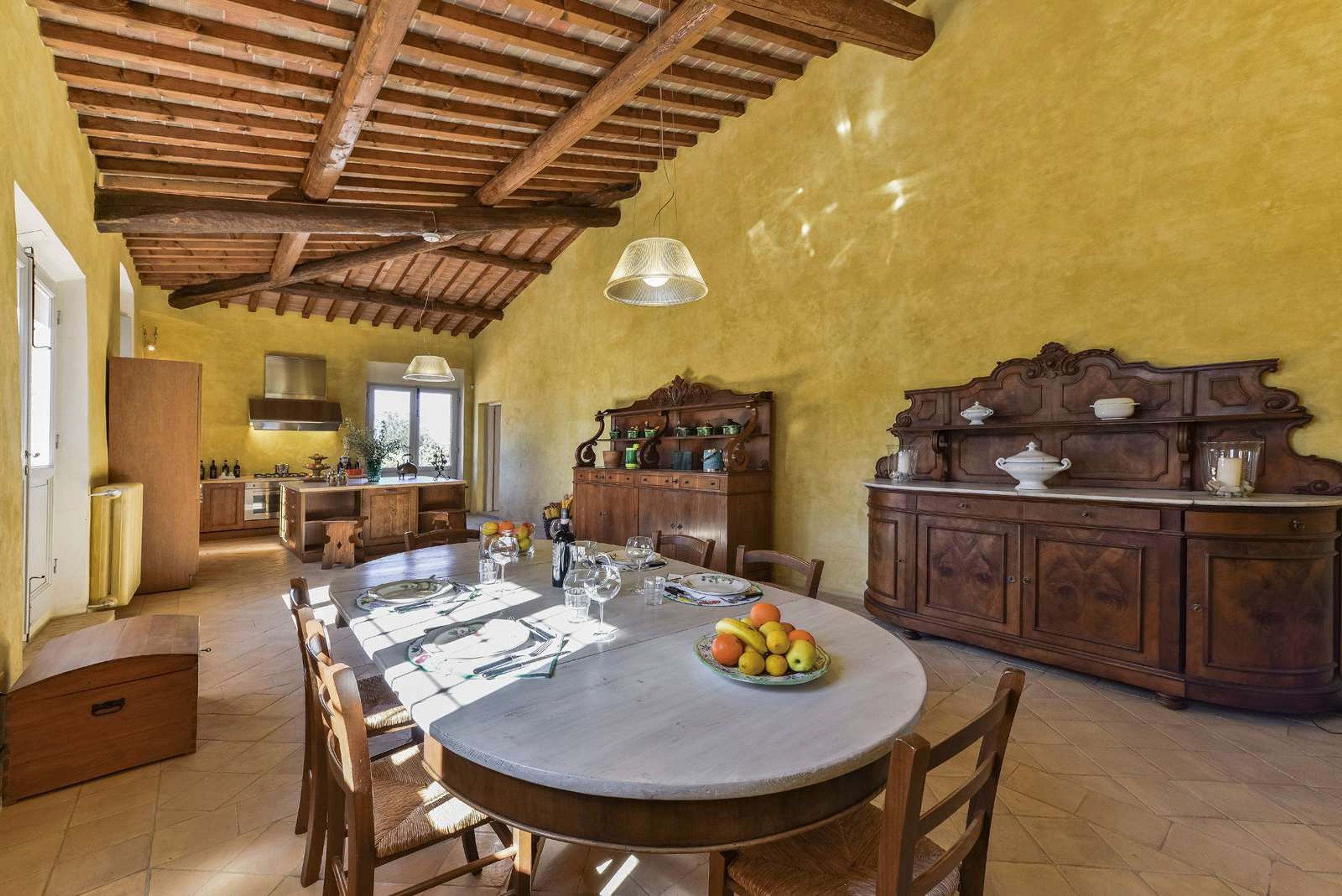 A rustic kitchen with a wooden ceiling, a round dining table set for four, and a fruit bowl on the table.