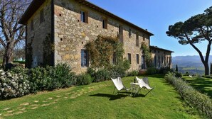 A stone building with a garden, two white chairs, and a view of the landscape. - New Historic Tuscany Country House Retreat in a Vineyard Near Siena Villa Chiantissimo (Castelnuovo Berardenga)